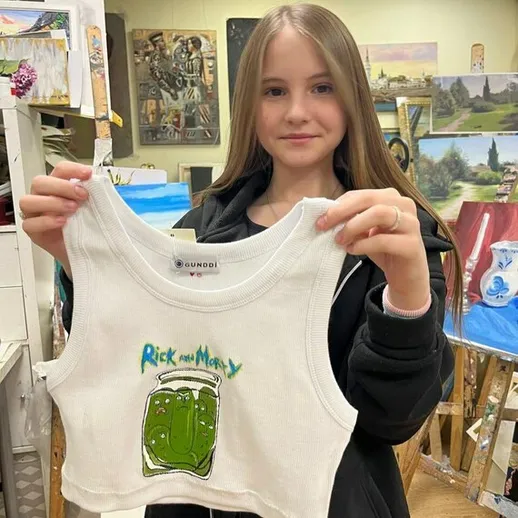 Девочка демонстрирует модный топ с изображением персонажей из мультфильма в художественной мастерской
