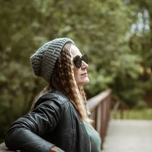 Женщина в шапке и солнцезащитных очках на мосту в парке в летний день