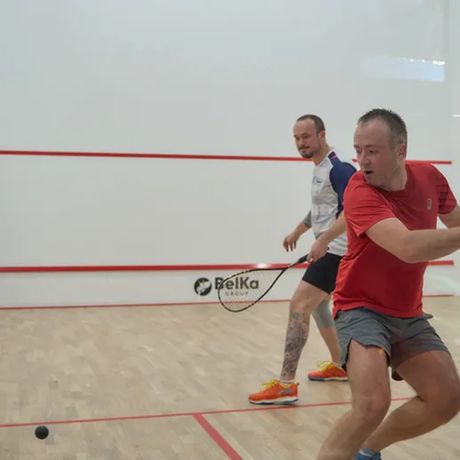 Два человека играют в сквош в спортзале, сосредоточенные на игровом процессе и демонстрирующие отличную технику