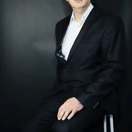 Серьезный мужчина в деловом костюме сидит на стуле на темном фоне во время фотосессии