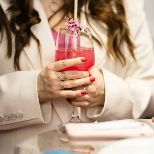 Женщина в светлом пиджаке держит коктейль с цветами на праздничной вечеринке