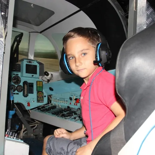 Мальчик в кабине пилота симулятора, вдохновленный авиацией, позирует в игровой зоне в летнее время