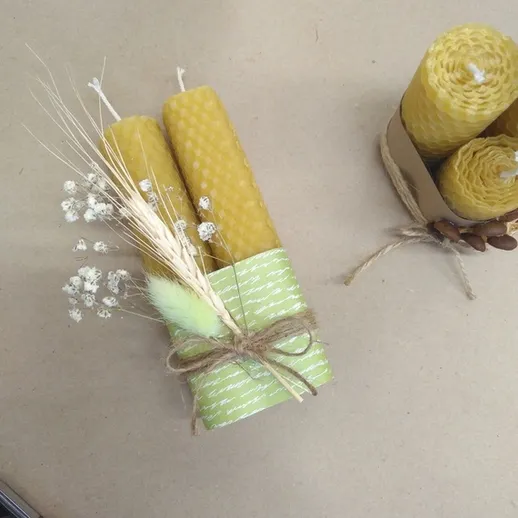 Два зеленых восковых свечи с украшением из трав и цветами на столе