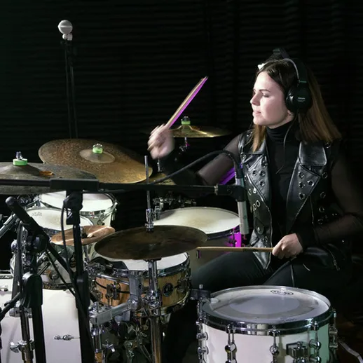 Молодая девушка играет на барабанах в учебной студии, сосредоточенная и увлеченная процессом музыки