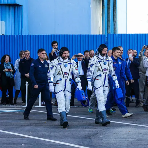 Астронавты в скафандрах выходят на улицу к ожидающим зрителям в космическом центре накануне запуска