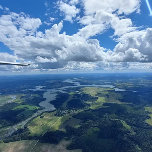 Вид с высоты на извивающиеся реки и зелёные поля под облачным небом