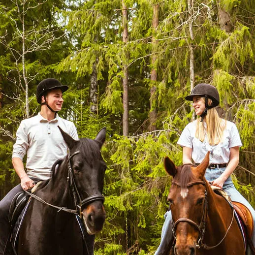 Молодая пара верхом на лошадях в лесу, наслаждающаяся природой в солнечный день Молодая пара верхом на лошадях в лесу, наслаждающаяся природой в солнечный день