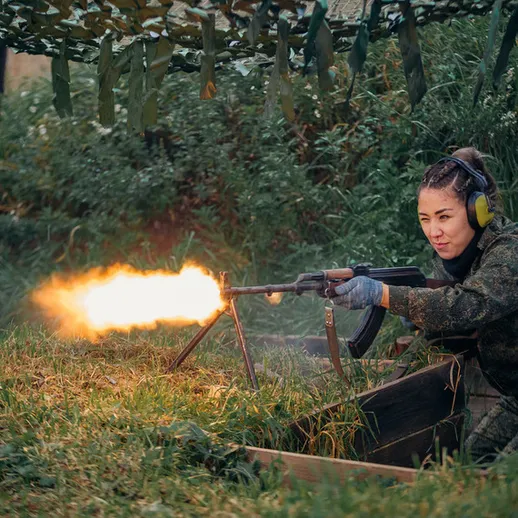 Женщина-военнослужащая стреляет из оружия на учениях в лесу во время золотой осени