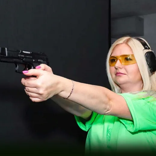 Женщина в защитных очках стреляет из пистолета на закрытом тире в дневное время